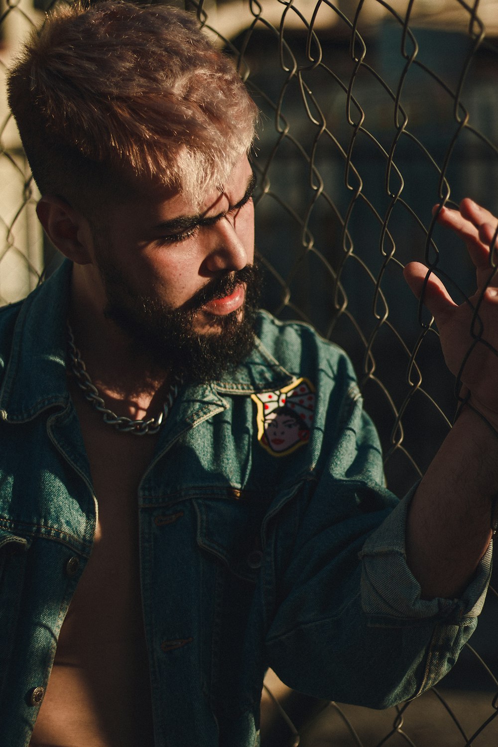 a shirtless man with a beard standing behind a fence