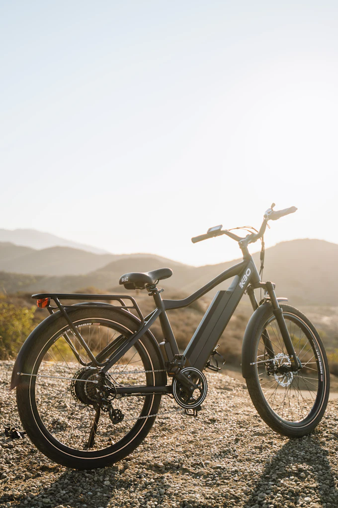 An electric bicycle standing on a gravel track with dry hills behind it in low sun.