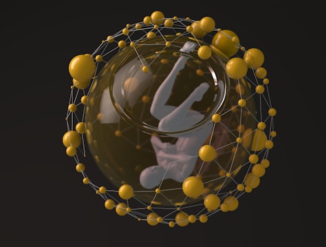 A humanoid figure suspended in a fetal position within a transparent sphere, surrounded by a network of interconnected yellow spheres. The structure resembles a scientific or futuristic representation.