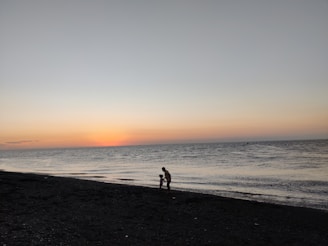 A serene photo of a father and child walking along a quiet beach at sunset.
