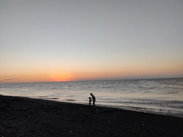 A serene Thai beach at sunset with a mother and child reading together on a woven mat.