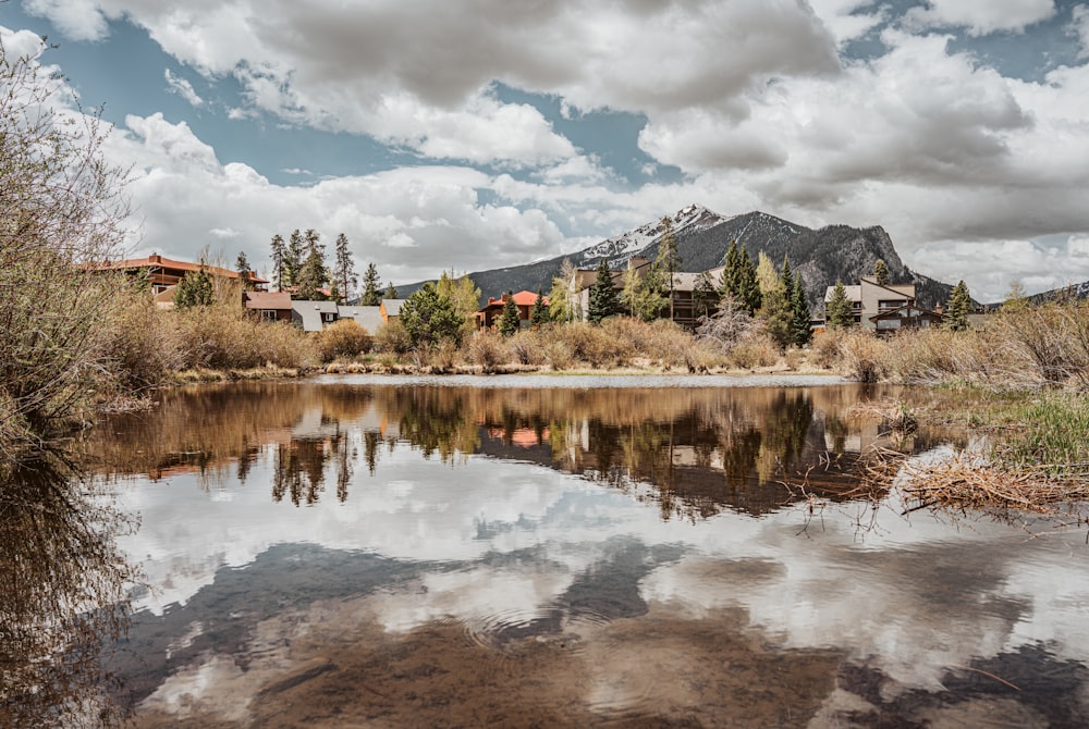 a lake surrounded by trees and mountains under a cloudy sky