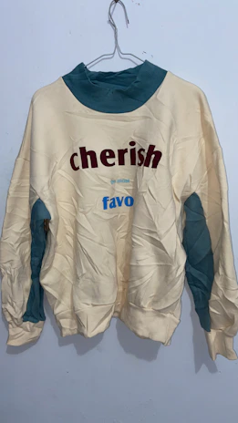 Vintage-style graphic sweatshirt with exclusive artwork displayed on a rustic wooden hanger against a cream wall.