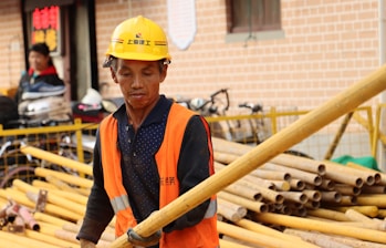 a man wearing a hard hat and carrying a large wooden stick