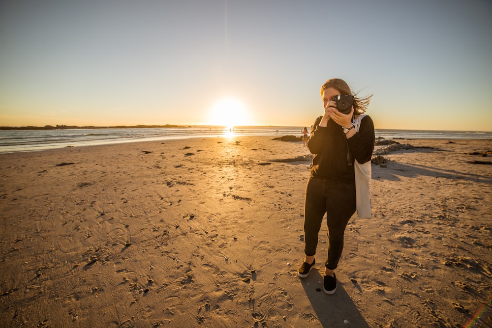 a woman taking a picture of the sun setting on the beach