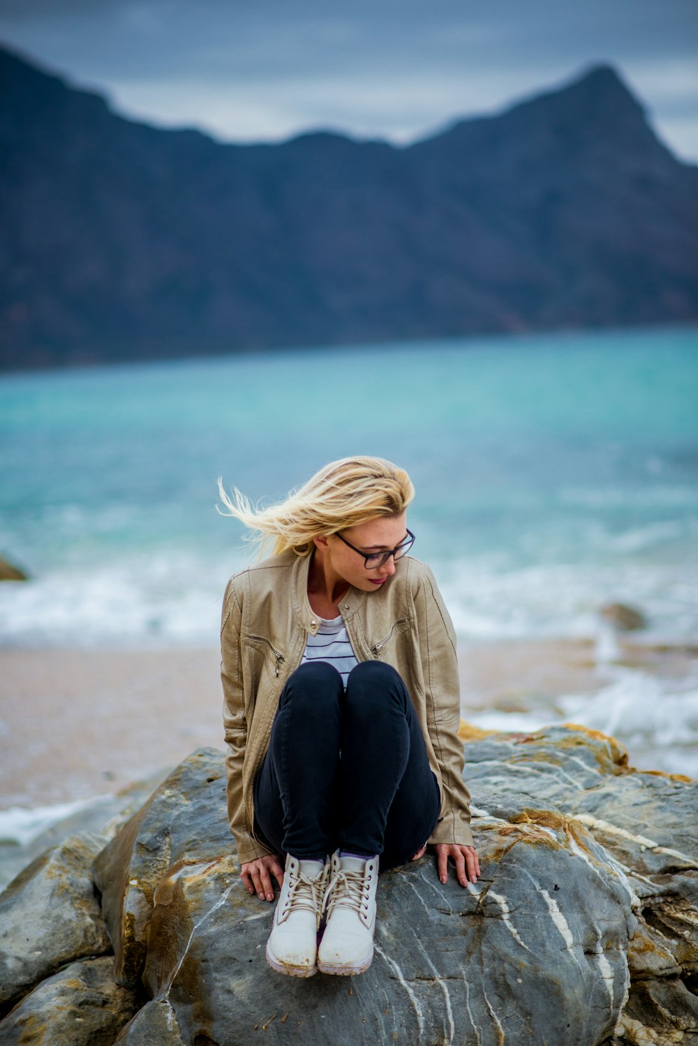 a woman sitting on top of a rock near the ocean