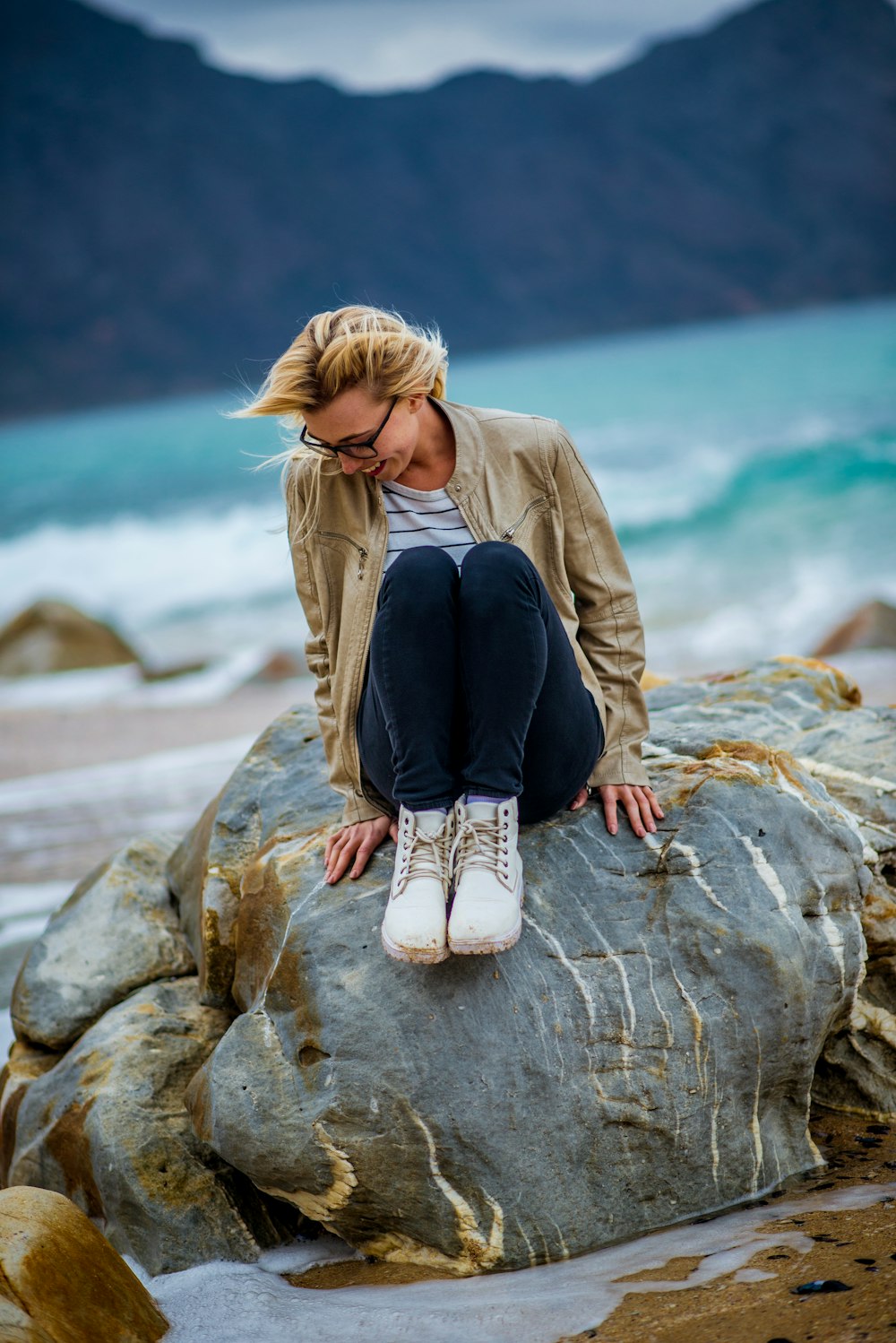 a woman sitting on top of a rock near the ocean