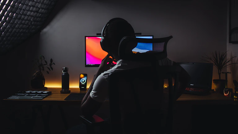 Photo of a tech nomad workspace with a laptop, headphones, and ambient neon lighting.