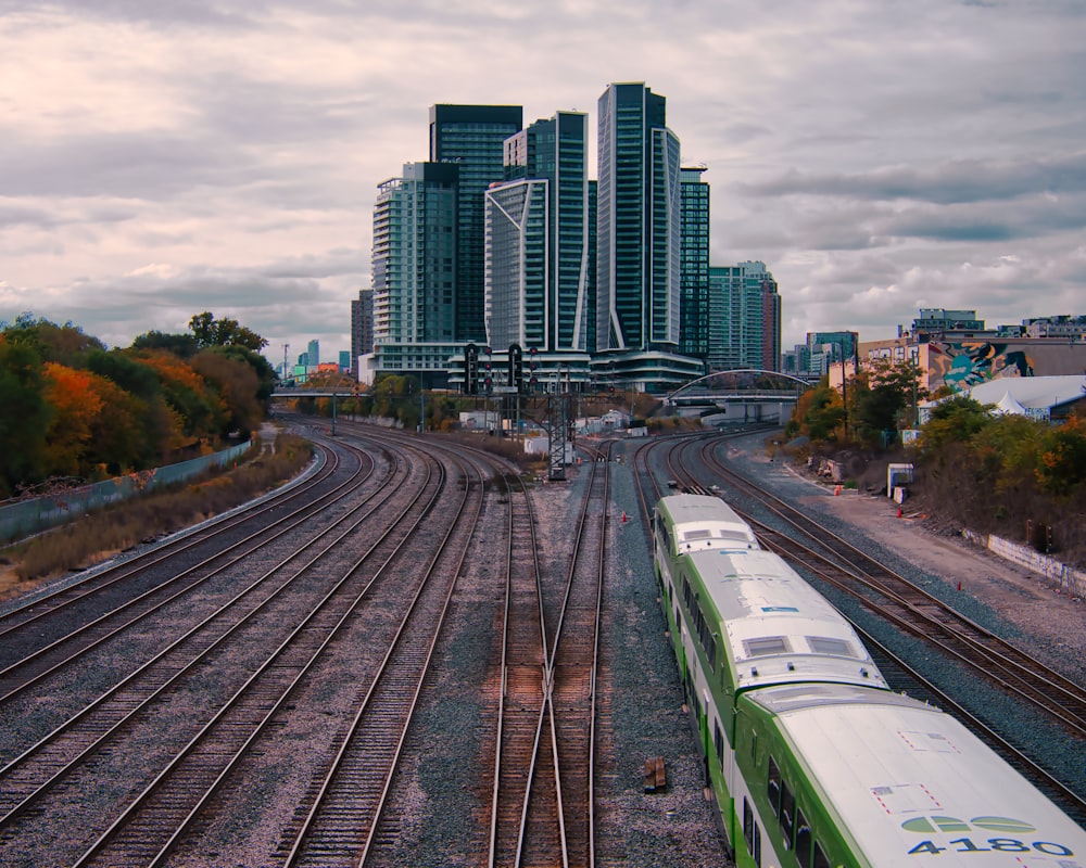 a green and white train traveling past tall buildings
