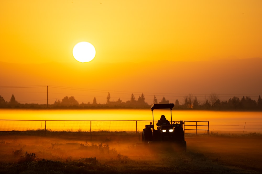 une personne conduisant un tracteur dans un champ au coucher du soleil