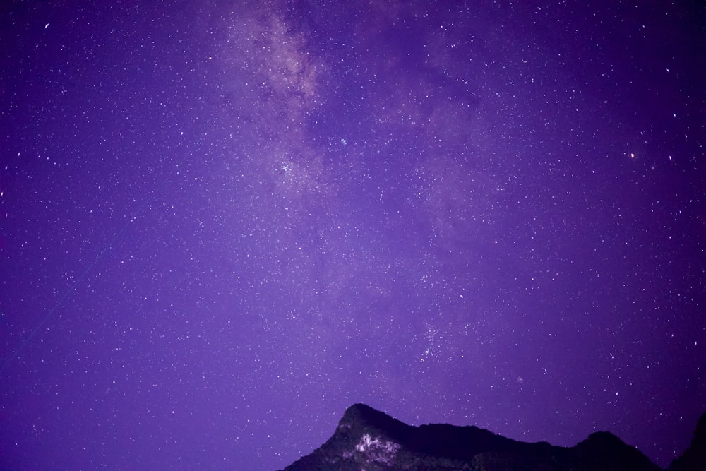 a mountain under a purple sky filled with stars