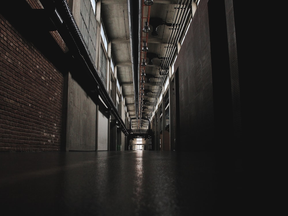 a dark hallway with exposed pipes and a brick wall