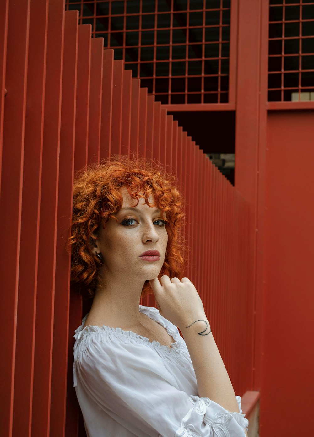 a woman with red hair leaning against a red wall