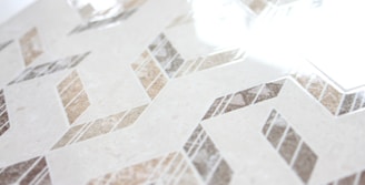 Geometric patterns with a combination of beige, brown, and gray tones create a zigzag design across a smooth surface. The glossy finish reflects light, adding a sense of elegance and modernity.