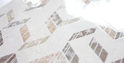 Geometric patterns with a combination of beige, brown, and gray tones create a zigzag design across a smooth surface. The glossy finish reflects light, adding a sense of elegance and modernity.