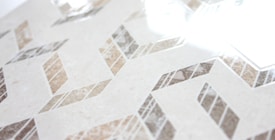 Geometric patterns with a combination of beige, brown, and gray tones create a zigzag design across a smooth surface. The glossy finish reflects light, adding a sense of elegance and modernity.