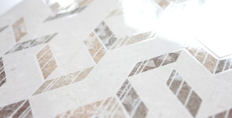 Geometric patterns with a combination of beige, brown, and gray tones create a zigzag design across a smooth surface. The glossy finish reflects light, adding a sense of elegance and modernity.