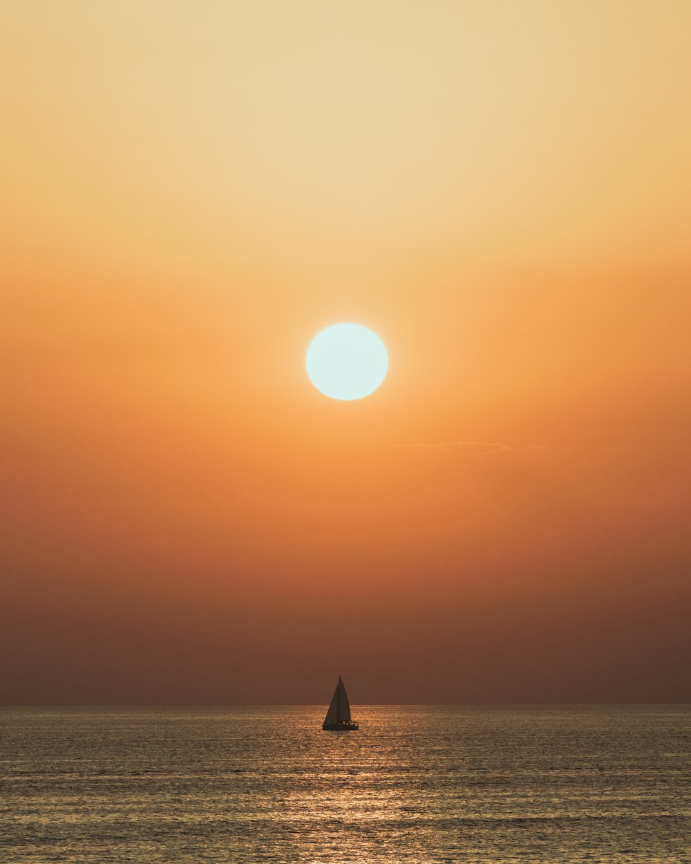 the sun is setting over the ocean with a sailboat in the foreground