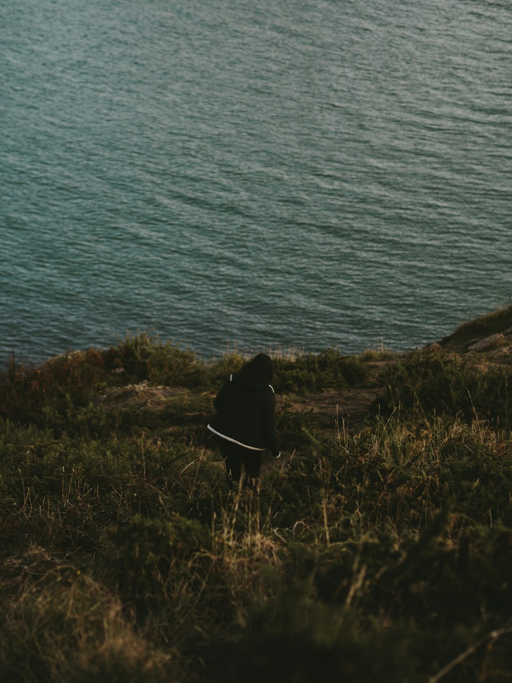 uma pessoa sentada em uma colina com vista para um corpo de água