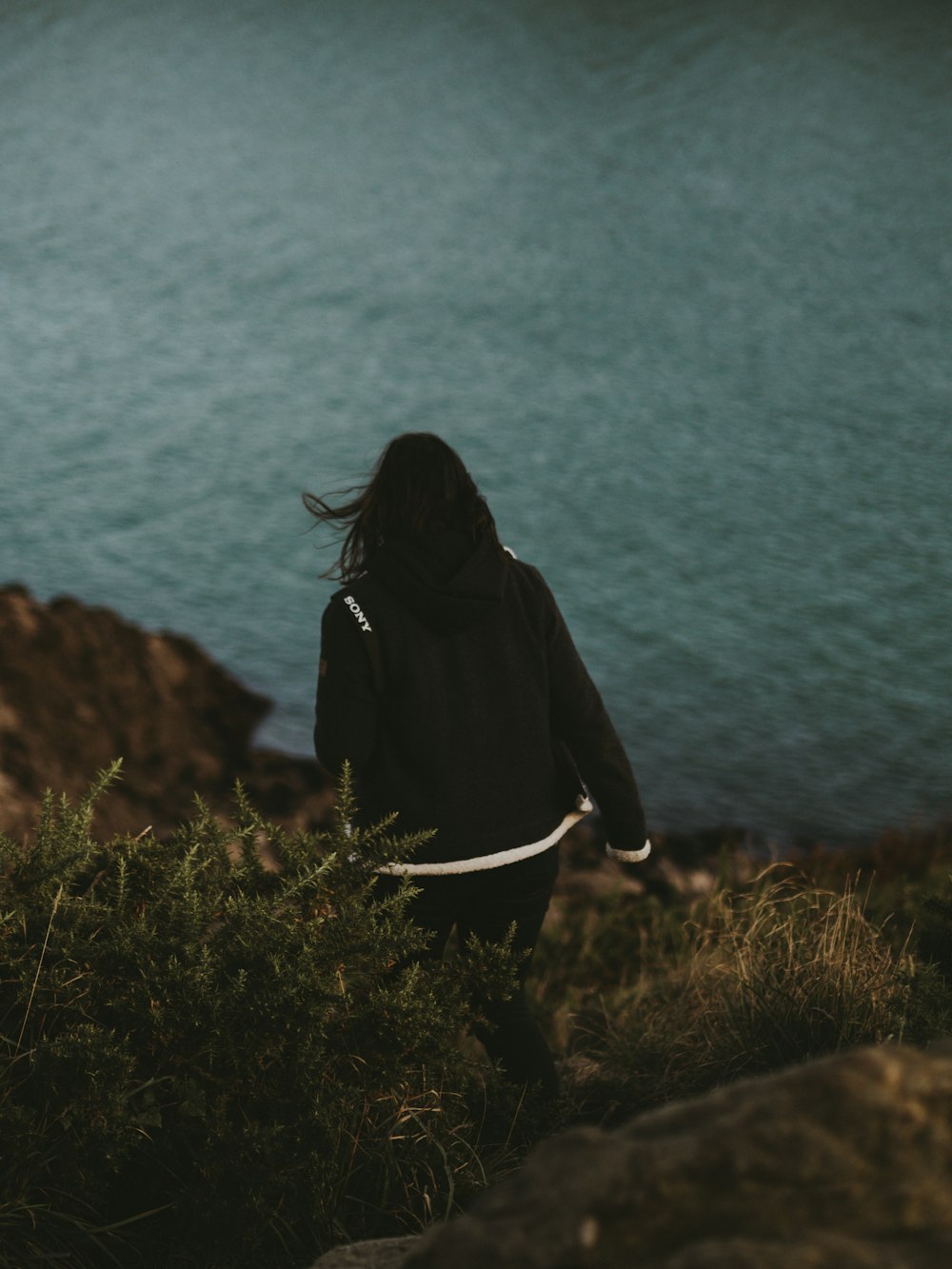 a woman walking up a hill next to a body of water