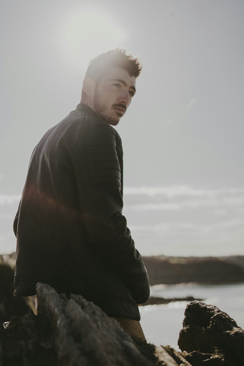 a man is sitting on a rock by the water