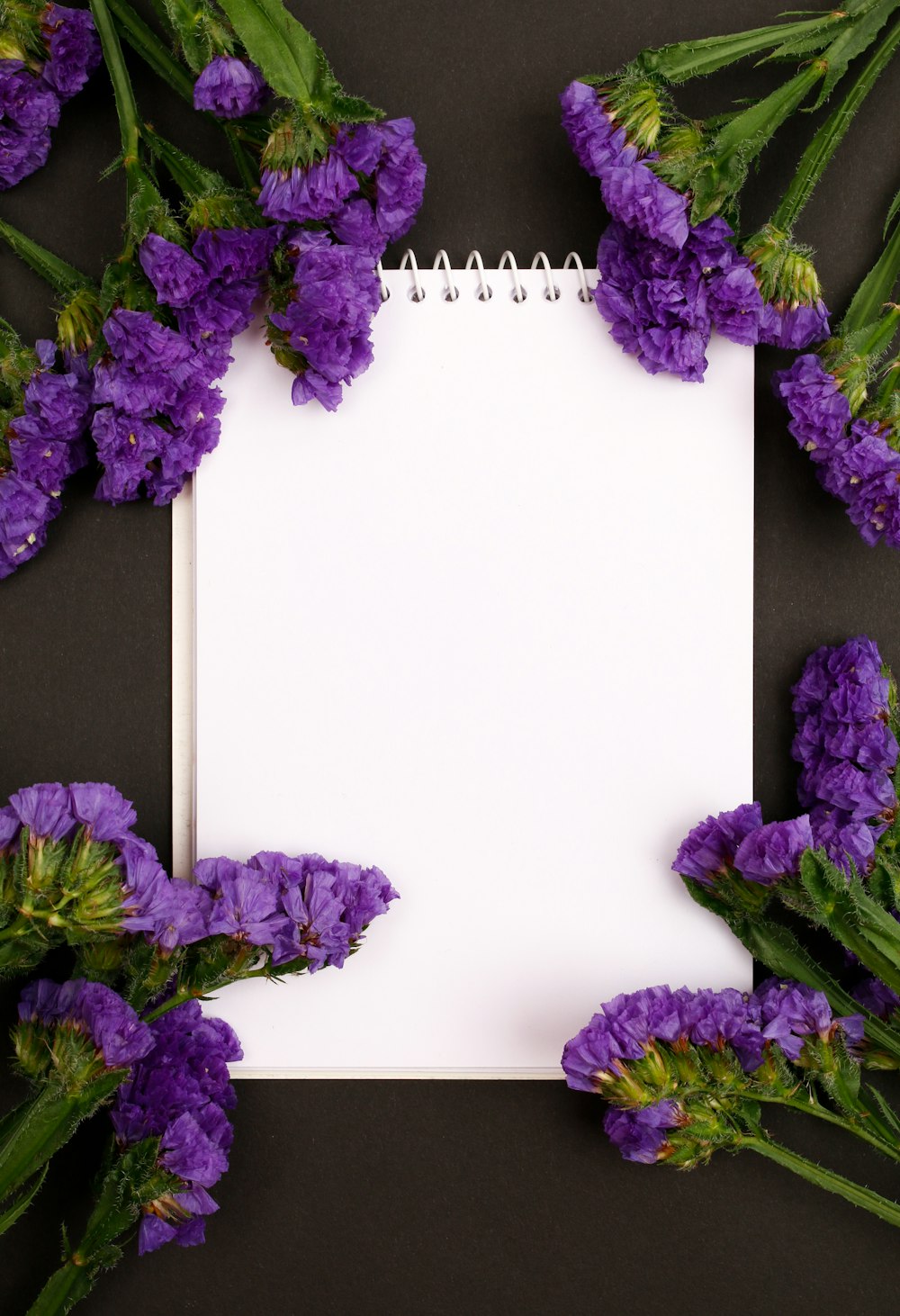 a notepad surrounded by purple flowers on a black background