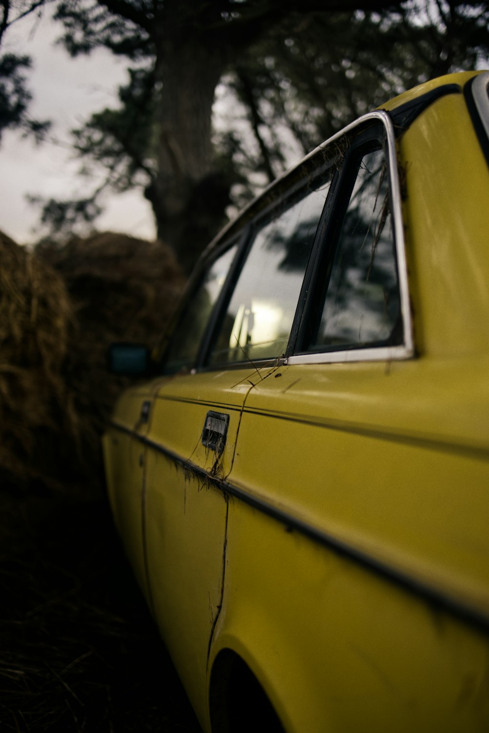 a yellow car parked next to a pile of hay