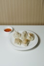 a white plate topped with dumplings next to a bowl of dipping sauce