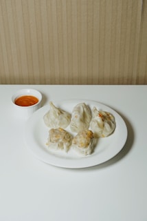 a white plate topped with dumplings next to a bowl of dipping sauce