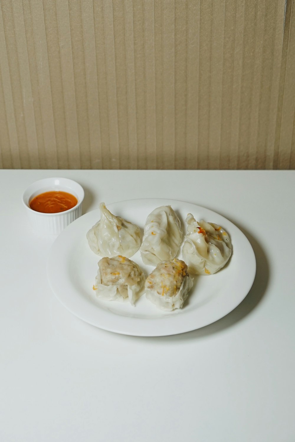a white plate topped with dumplings next to a bowl of dipping sauce