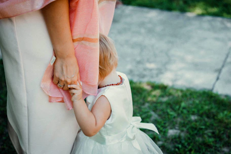 a little girl in a white dress is holding her mother's hand