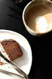 a piece of cake on a plate next to a cup of coffee