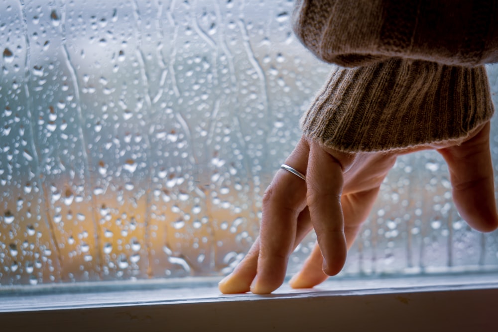 a person's hand on a window sill with rain drops