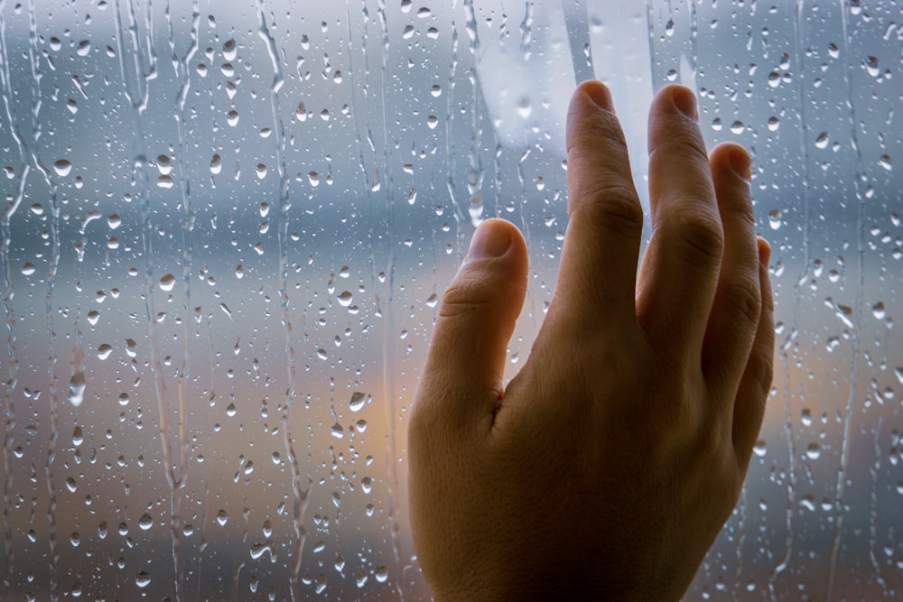 die Hand einer Person an einem Fenster mit Regentropfen