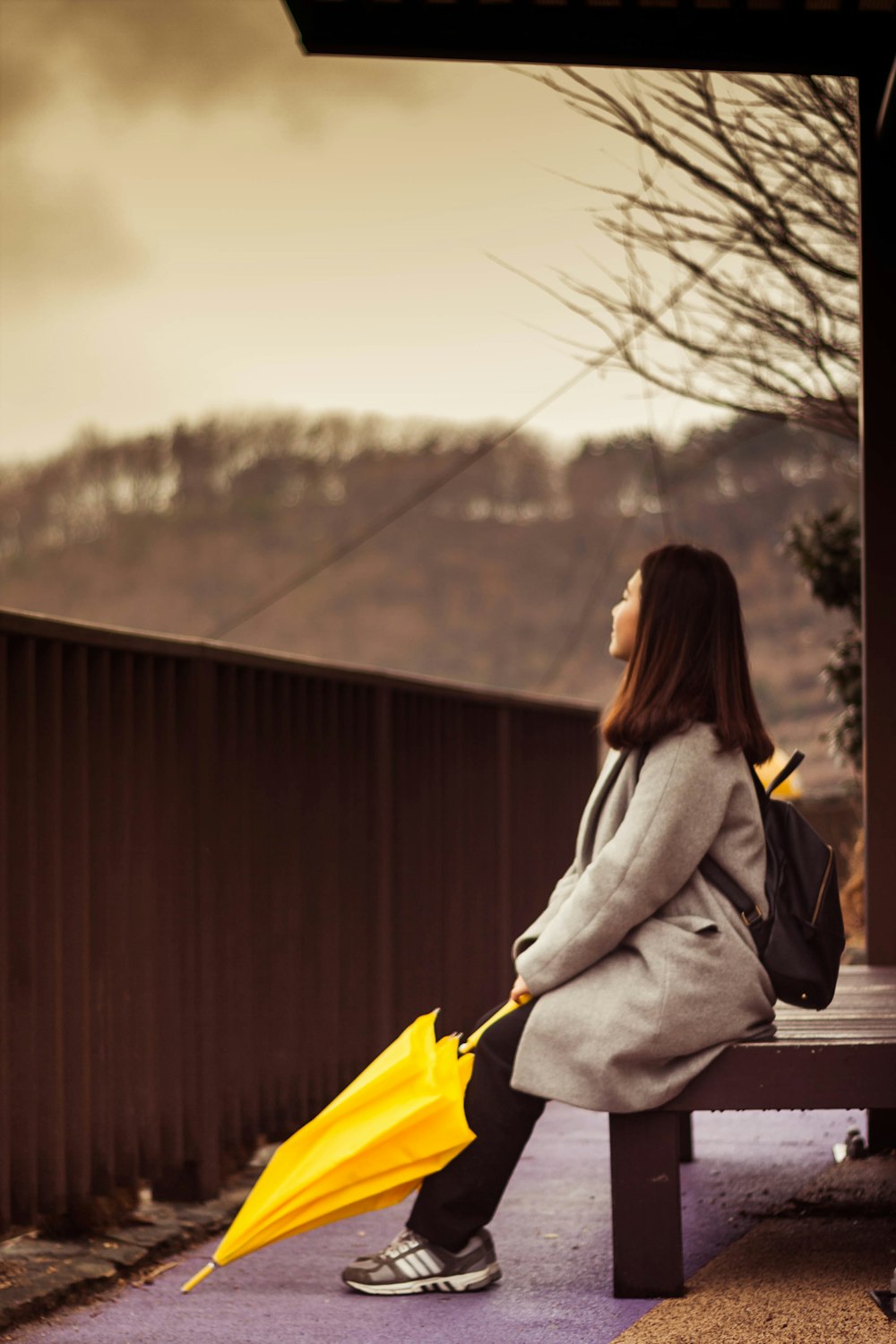 una donna seduta su una panchina che tiene un ombrello giallo