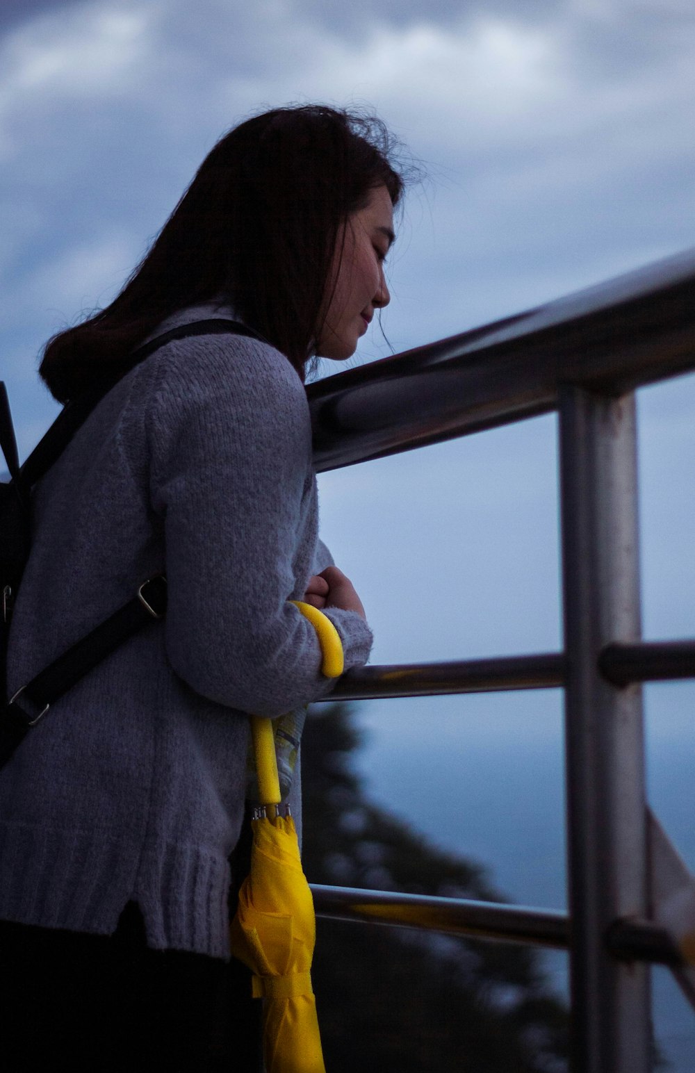 a woman holding a yellow umbrella standing next to a railing