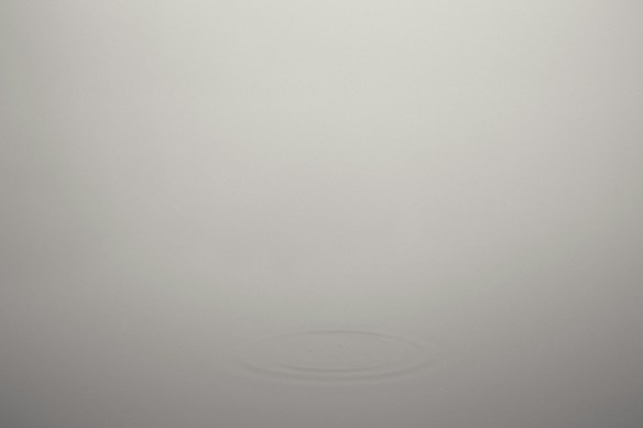 A minimalistic scene with a soft gray background and a subtle ripple effect in the center, creating a sense of calm and simplicity.