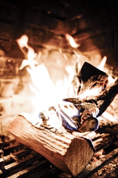 A fireplace with burning logs and bright flames, surrounded by a brick background. The fire emits warm, orange and yellow colors, creating a cozy ambiance.
