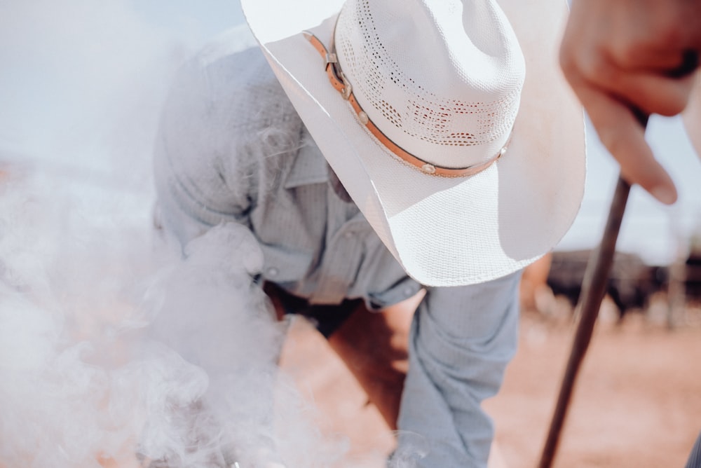a man in a white cowboy hat bending over with a stick