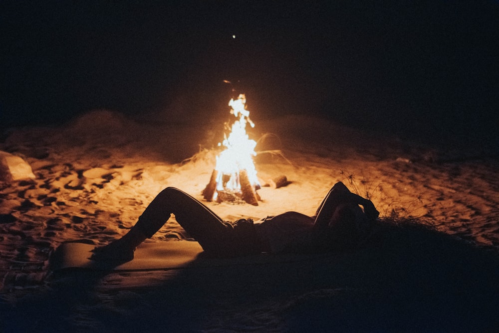 a woman is sitting in front of a campfire