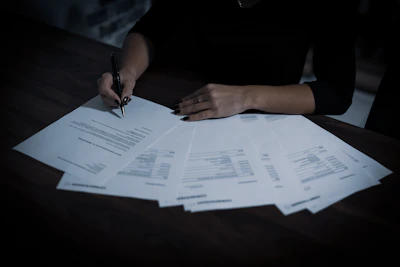 Close-up of hands reviewing real estate documents over a wooden table.