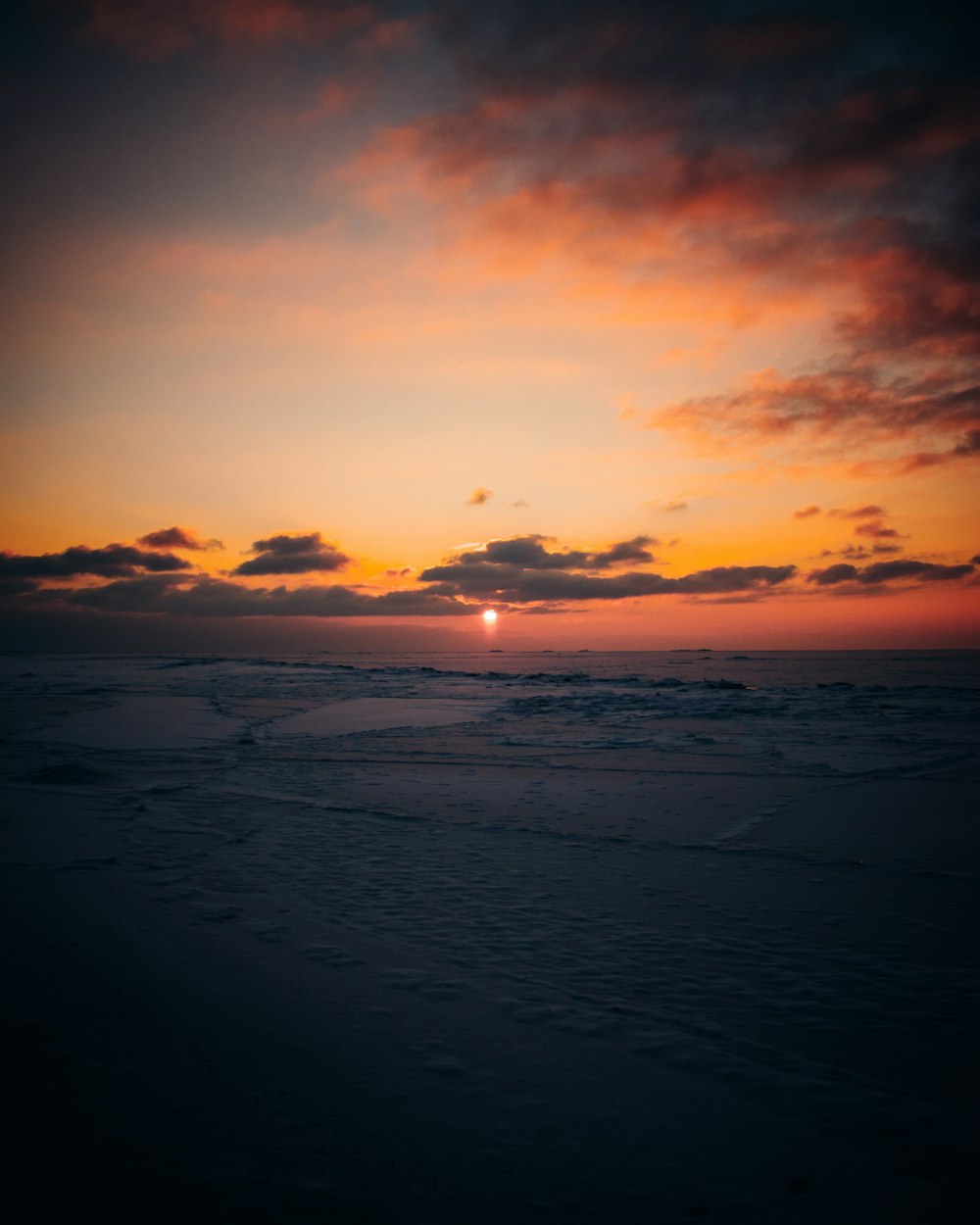 the sun is setting over the ocean on a cloudy day