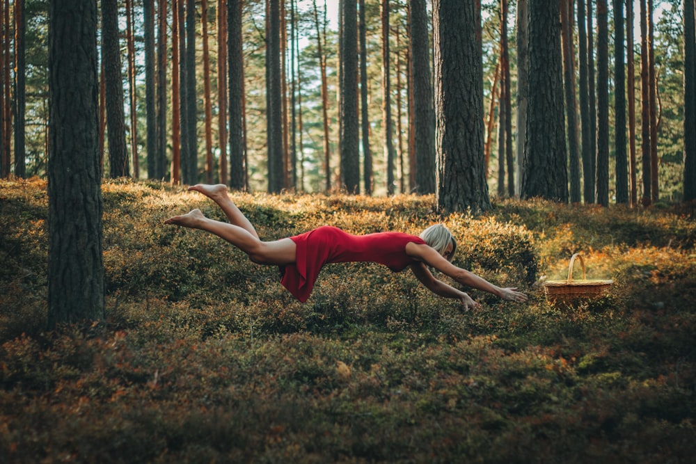 a woman in a red dress laying on the ground in a forest