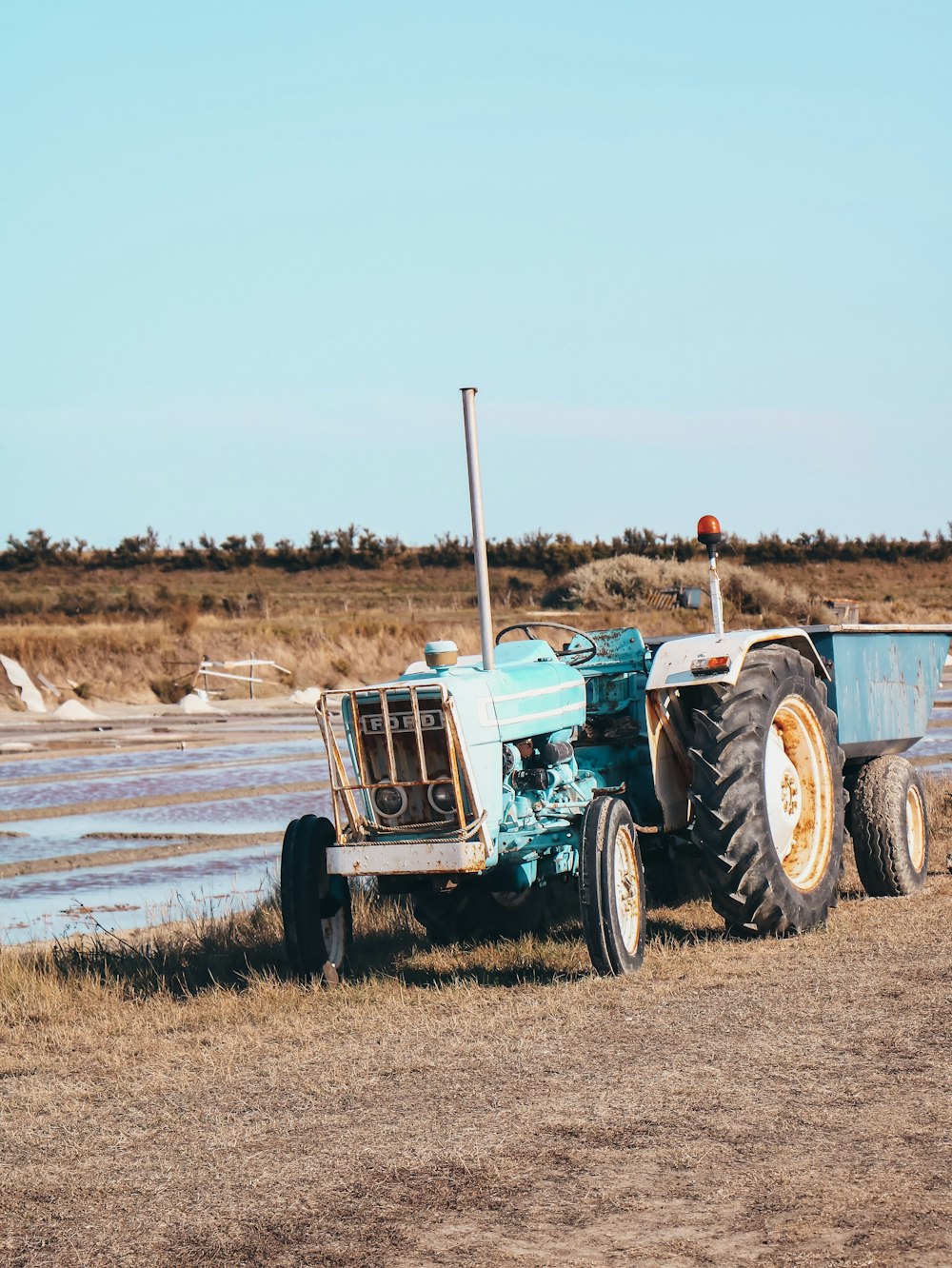 Un tractor azul estacionado en un campo junto a un cuerpo de agua