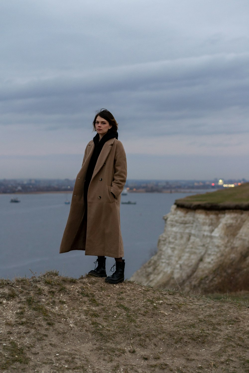 a woman standing on top of a hill next to a body of water