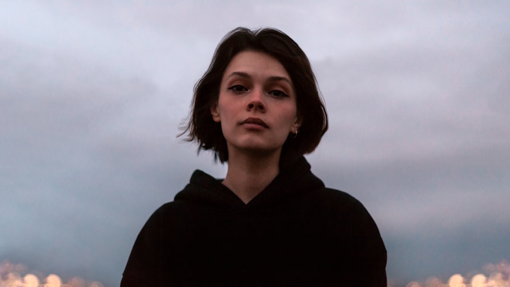 a woman in a black hoodie looking up at the sky