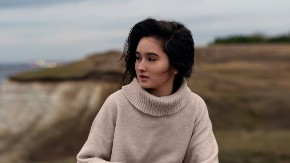 a woman in a turtle neck sweater looking off into the distance