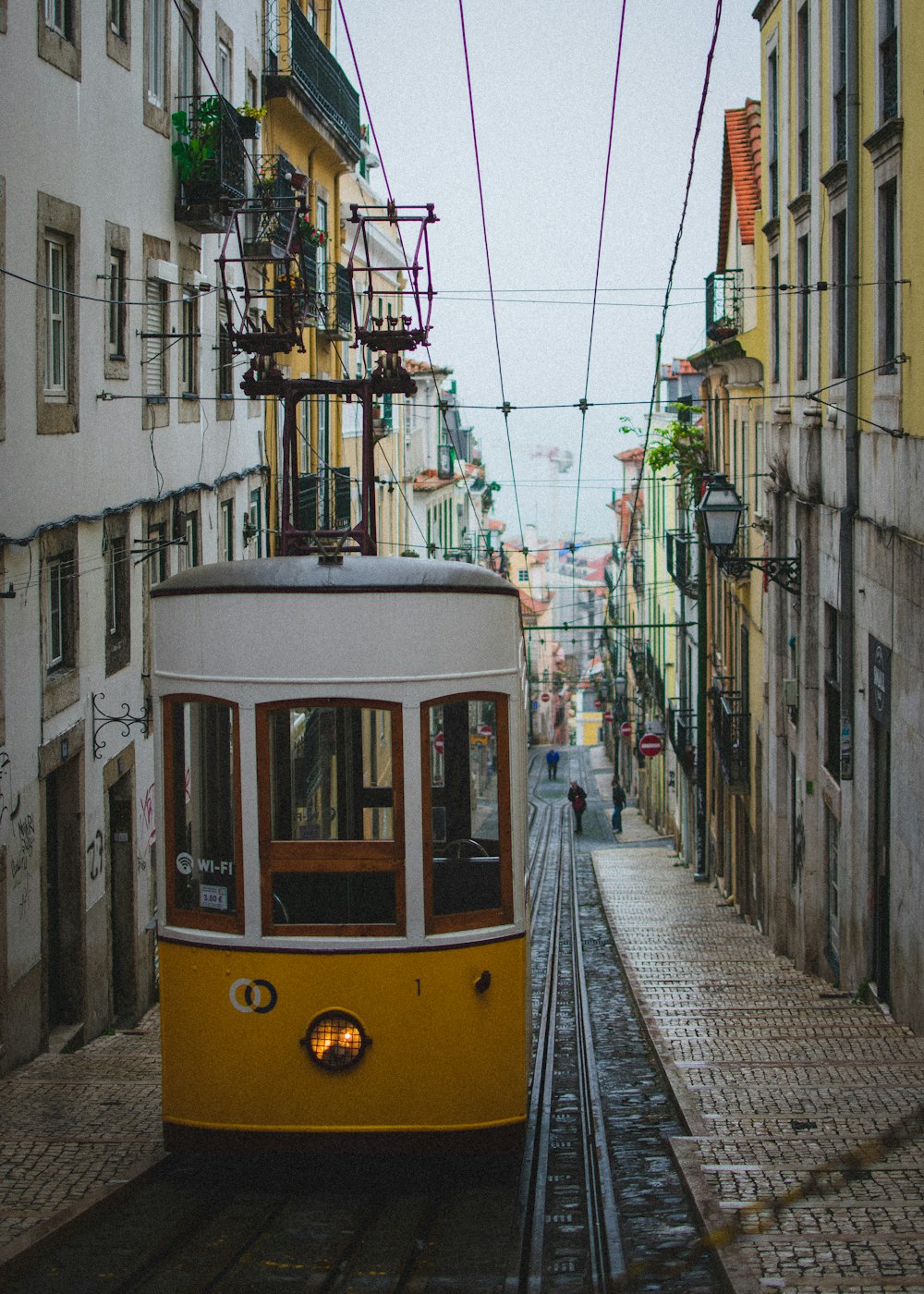 a yellow trolley car traveling down a street next to tall buildings