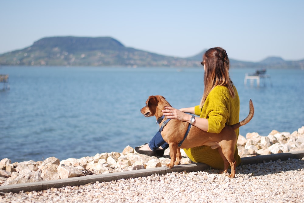 a woman sitting next to a dog on a beach