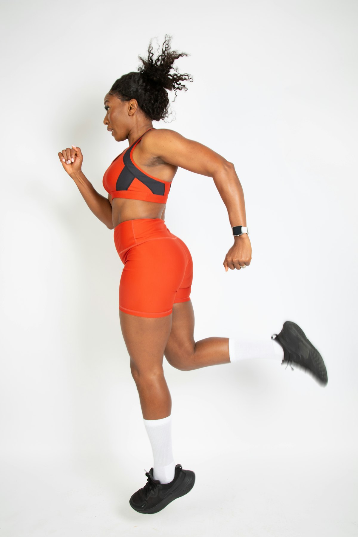 A runner in an orange kit mid-stride in a white studio
